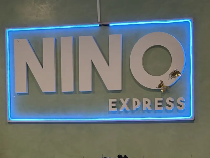 El cartel de adentro: las letras blancas de Nino Express sobre la pared verde, con luz azul alrededor